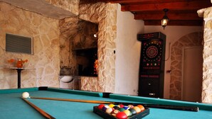 Une table de billard avec un queue et des billes, un jeu de fléchettes et un mur en pierre.