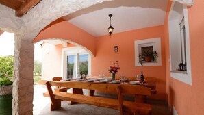 Un coin repas avec une table en bois dressée pour quatre personnes, un pilier en pierre et une plante en pot accrochée au mur.