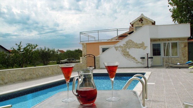 Un espace aménagé au bord de la piscine, avec une table, deux verres et une carafe contenant une boisson rouge.