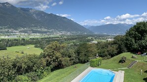 A pool surrounded by lush greenery and mountains in the background. - 4* Vacation Home Residenza Christa - Casa Wiro (Magadino - Gambarogno)