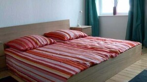 Ein Bett mit gestreifter Bettwäsche in einem Zimmer mit einem Holz-Kopfteil, einem Nachttisch und einem Fenster mit Vorhängen.