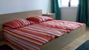 Ein Bett mit gestreifter Bettwäsche in einem Zimmer mit einem Holz-Kopfteil, einem Nachttisch und einem Fenster mit Vorhängen.