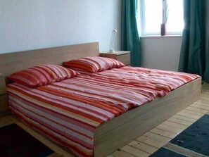 Un letto con lenzuola a righe in una stanza con una testiera in legno, un comodino e una finestra con tende.