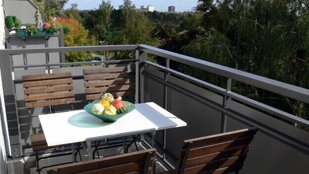 Ein Balkon mit Tisch und Stühlen, einer Obstschale und Blick auf Bäume und Gebäude.