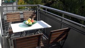 Ein Balkon mit Tisch und Stühlen, einer Obstschale und Blick auf Bäume und Gebäude.