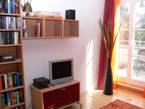 Un soggiorno con TV su un supporto in legno, una libreria piena di libri, un armadietto rosso e un'ampia finestra con vista sull'esterno.