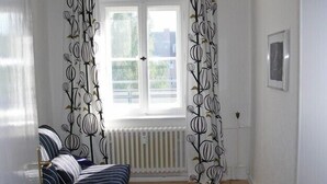 Ein Zimmer mit Fenster, Heizkörper, einem gestreiften Sofa und gemusterten Vorhängen.