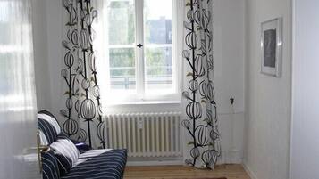 Ein Zimmer mit Fenster, Heizkörper, einem gestreiften Sofa und gemusterten Vorhängen.