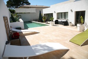 A modern outdoor patio with a swimming pool, lounge chairs, and potted plants.