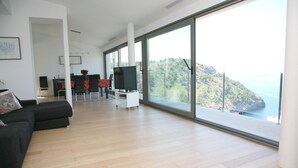 A spacious living room with a large TV, a dining area with chairs, and a view of the sea. - MODERN villa with pool and fantastic sea views.  (PUERTO DE SOLLER, MALLORCA)