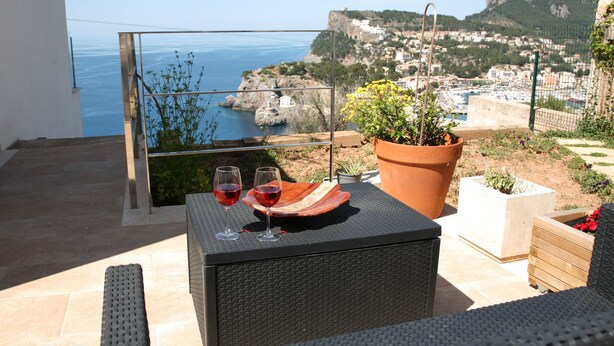 A balcony with a table, two glasses of red wine, a potted plant, and a view of the sea and town. - MODERN villa with pool and fantastic sea views.  (PUERTO DE SOLLER, MALLORCA)