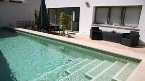 A swimming pool with clear water, a sunshade, outdoor furniture, and a modern building with large windows. - MODERN villa with pool and fantastic sea views.  (PUERTO DE SOLLER, MALLORCA)