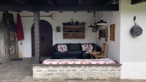 Un interior rústico con un banco de piedra, un sofá de color oscuro con cojines florales y una puerta de madera con un arco decorativo.