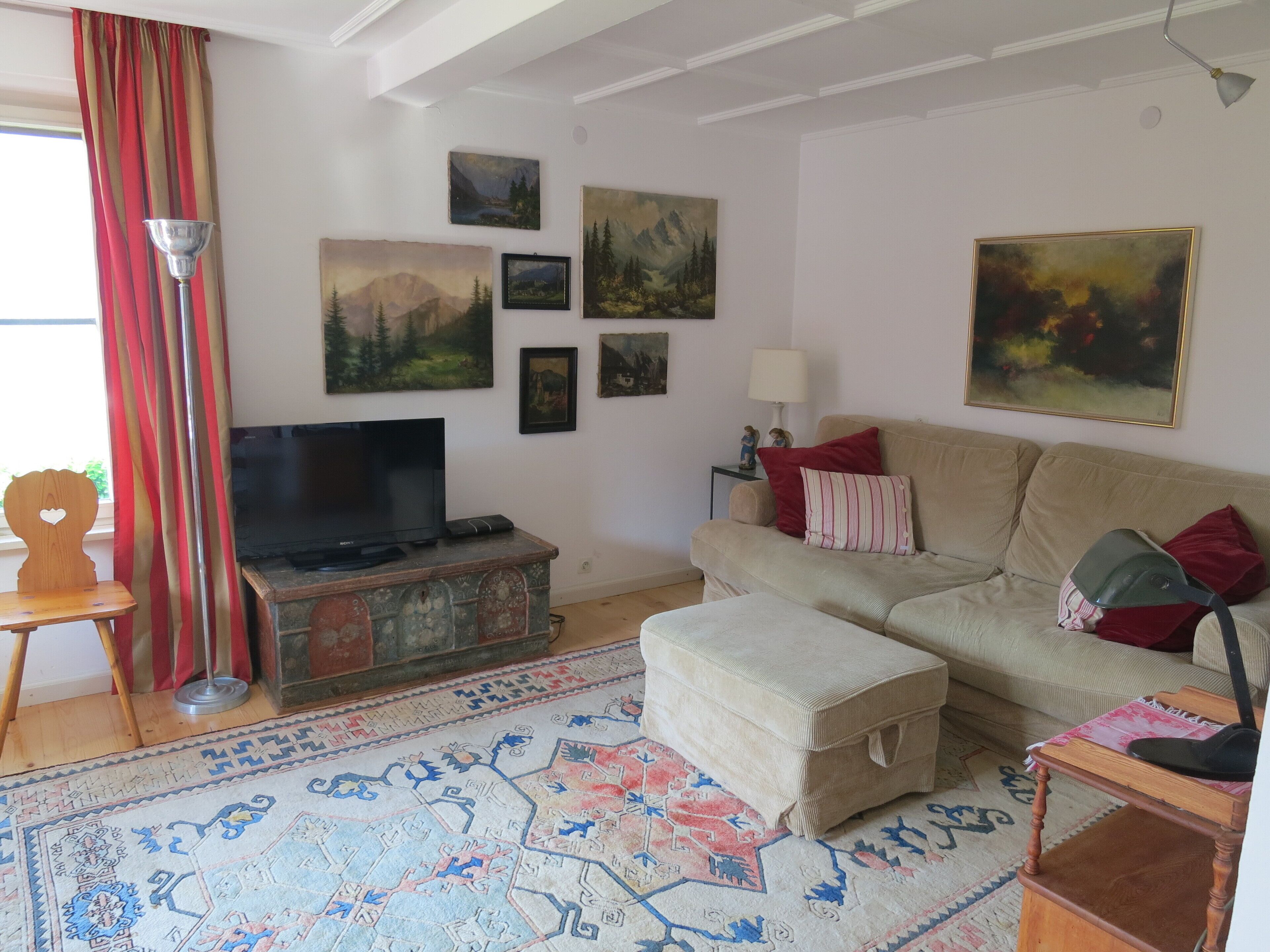 A living room with a sofa, ottoman, TV, and artwork on the wall.