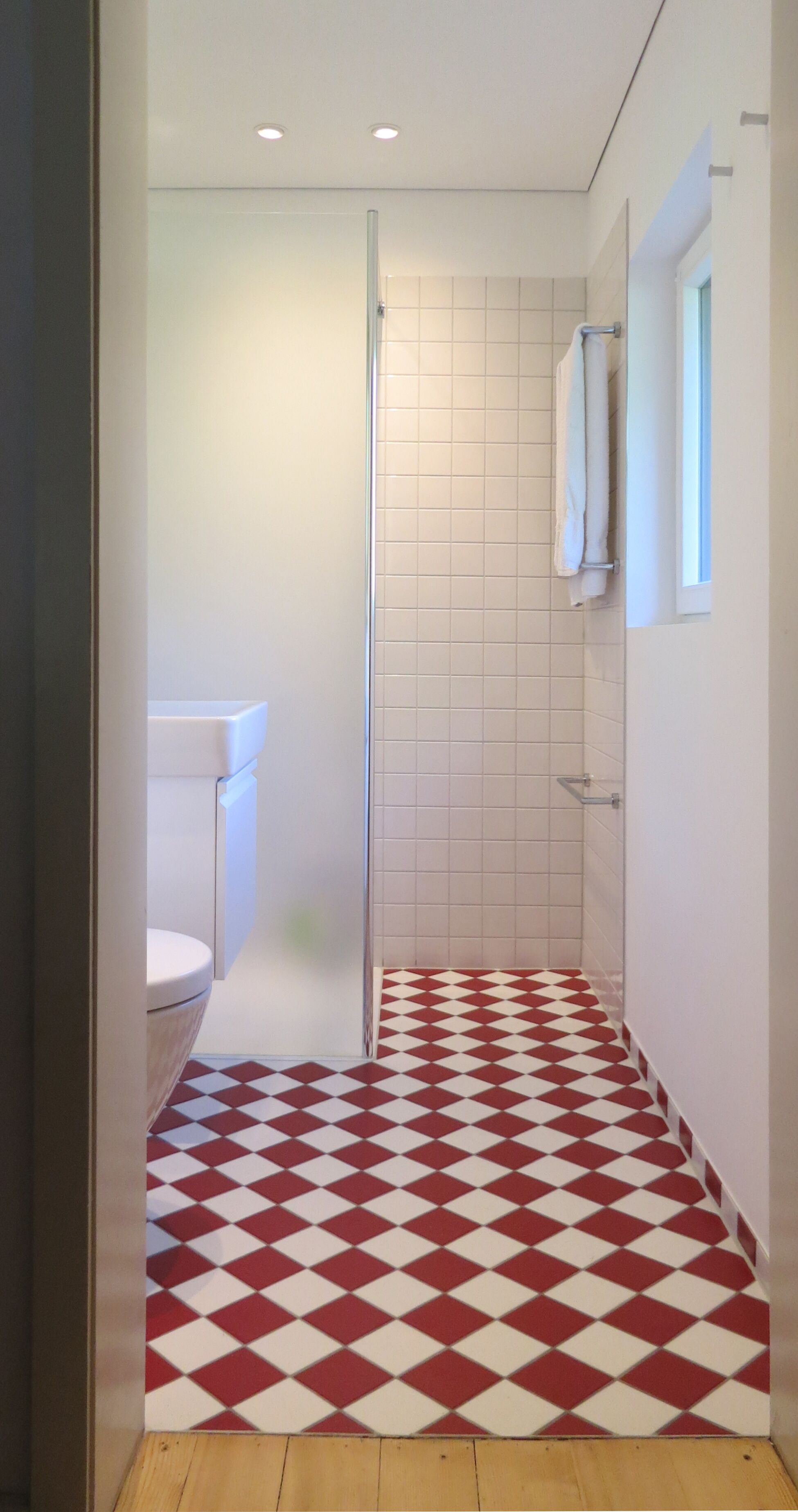 A bathroom with a red and white checkered floor, a white toilet, and a glass shower enclosure.