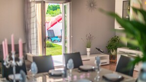 Een eetgedeelte met een tafel voor vier personen, een glazen schuifdeur die leidt naar een buitenruimte met een rode parasol, en een bloempot ernaast.