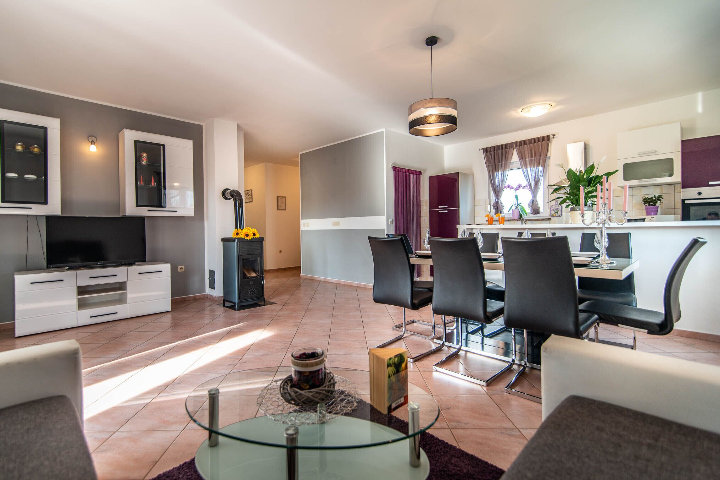 A modern living room with a glass coffee table, a flat-screen TV, and a dining area with a table and chairs.