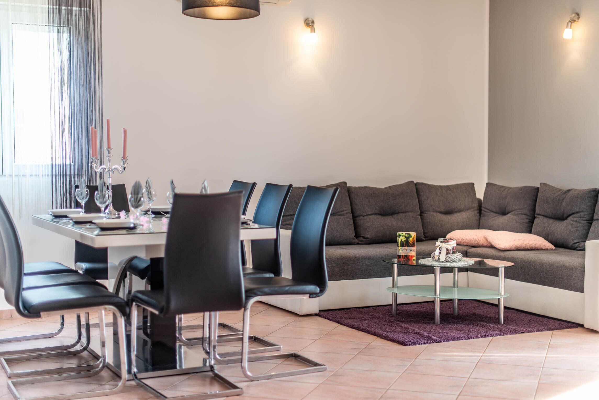 Un salon moderne avec un coin repas, comprenant un canapé, des fauteuils, une table basse et une table à manger décorée de bougies.