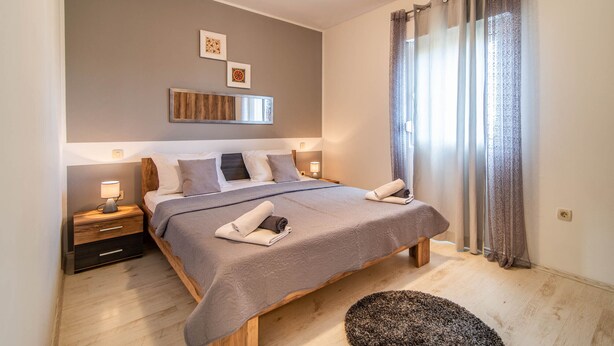 Een moderne slaapkamer met een groot bed, nachtlampjes en een uitzicht op de omgeving door dunne gordijnen.