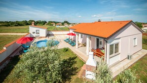 Een huis met een zwembad, buitenmeubels en een rode parasol.