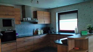 A kitchen with wooden cabinets, a built-in oven, a window with blinds, and a small shelf with a plant. - Luxurious, spacious **** apartment on a farm - family friendly (Tann (Rhön))