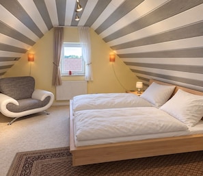 A bedroom with a bed, a chair, a window with curtains, and a radiator.