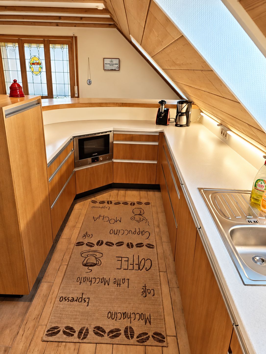 A compact kitchen with wooden cabinets, a built-in oven, a coffee machine, and a sink.