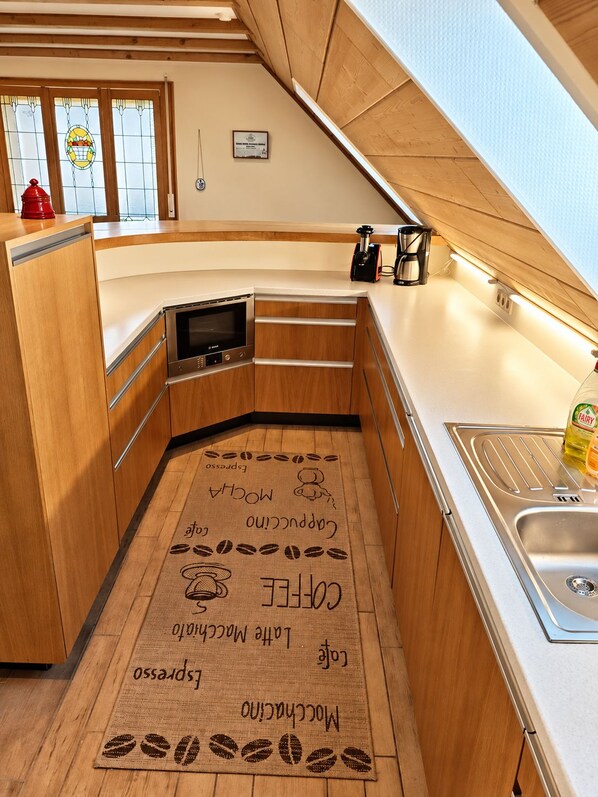 A compact kitchen with wooden cabinets, a built-in oven, a coffee machine, and a sink.