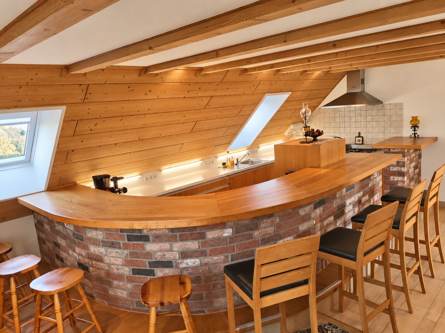 Una cocina con una isla de madera, taburetes de bar, pared de ladrillo y tragaluz.