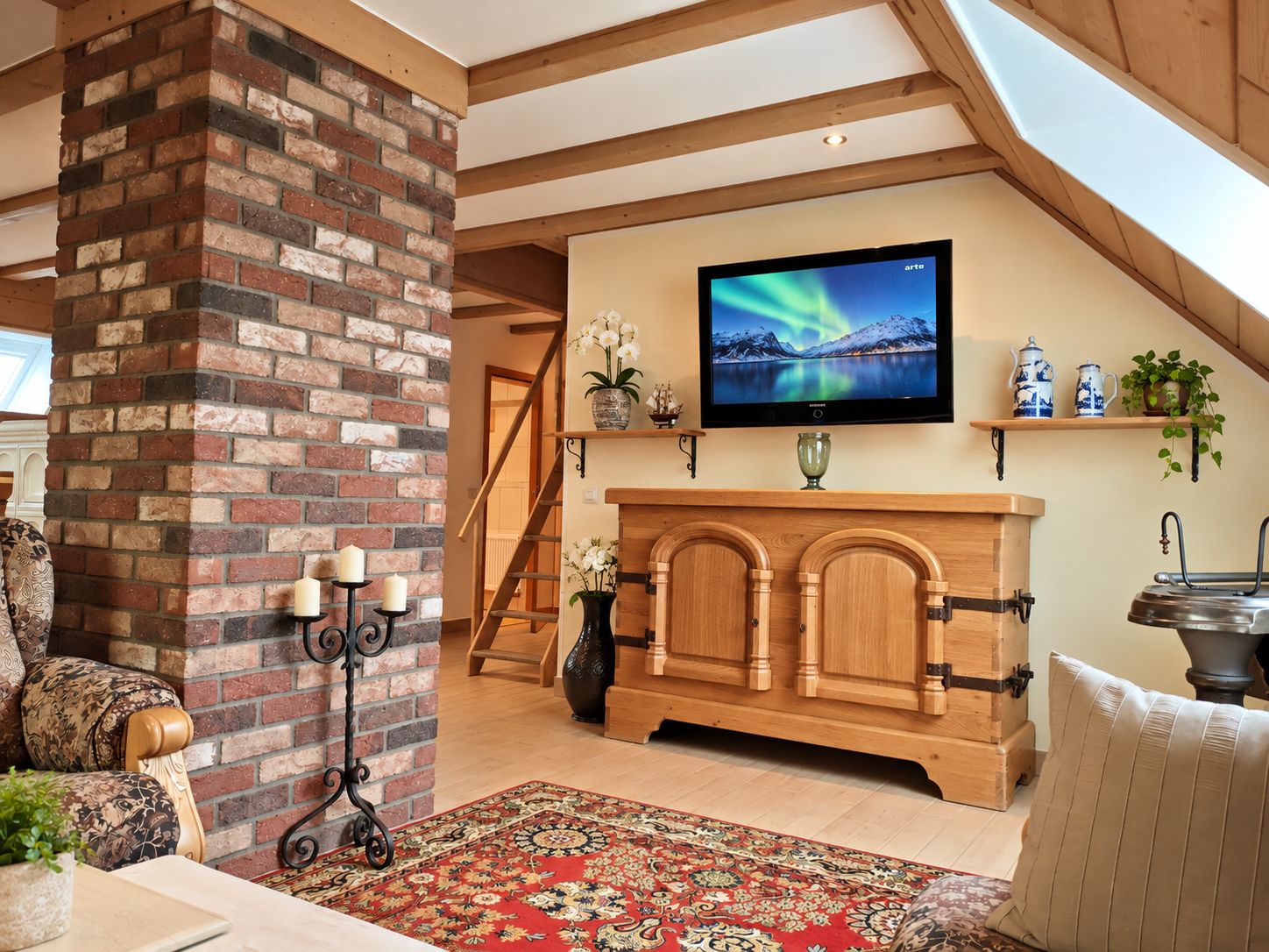 A cozy living room with a brick fireplace, a wooden cabinet, a television mounted on the wall, and a red patterned rug.