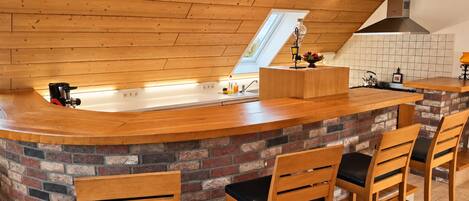 A kitchen with a wooden countertop, a brick backsplash, and a high ceiling with exposed beams.