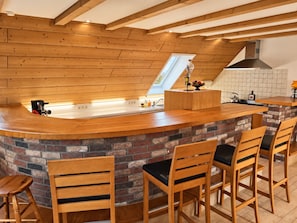 A kitchen with a wooden countertop, a brick backsplash, and a high ceiling with exposed beams.