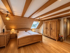 Un dormitorio con techo de madera, tragaluz, cama, mesitas de noche y armario.