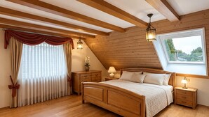 A bedroom with a sloped ceiling, wooden beams, a large bed, bedside tables, and a window with a view.
