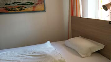 A single bed with a wooden headboard, a white pillow, and a colorful abstract painting on the wall.