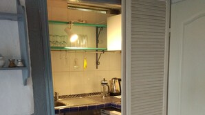 Cocina compacta con lavabo, hervidor y refrigerador. Se observa una silla y una repisa con utensilios de cocina.