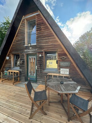 A wooden cabin with a sloped roof, a deck with outdoor seating, and a sign indicating a pharmacy.