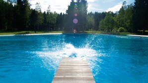 Una piscina con cubierta de madera en primer plano y un área boscosa al fondo.