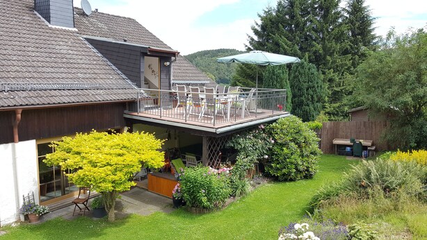 A two-story building with a balcony, a wooden deck, and a garden with various plants and flowers. - Frankfurt a. Experience M. - enjoy peace in the Taunus - children and dogs welcome (Schmitten)
