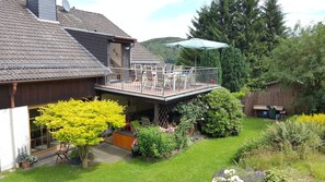 Een gebouw met twee verdiepingen, een balkon, een houten terras en een tuin met diverse planten en bloemen.
