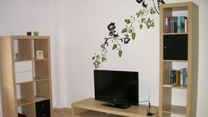 A living room with a TV on a wooden stand, a bookshelf, and a decorative wall decal. - Frankfurt a. Experience M. - enjoy peace in the Taunus - children and dogs welcome (Schmitten)