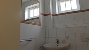 Ein Badezimmer mit weißen Fliesen, einem Waschbecken, einem Spiegel und einem Fenster.