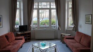 Ein Wohnzimmer mit zwei Sofas, einem Glastisch, einem Fernseher und einem Fenster mit Vorhängen.