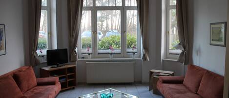 A living room with two sofas, a glass coffee table, a TV, and a window with curtains.
