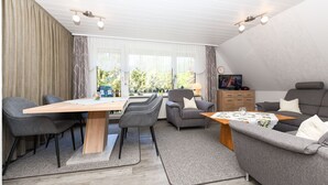 A modern living room with a wooden dining table, grey sofas, and a TV on a wooden cabinet.