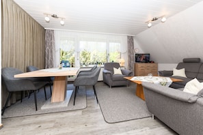 Ein modernes Wohnzimmer mit einem Holzespeisetisch, grauen Sofas und einem Fernseher auf einer Holzkommode.