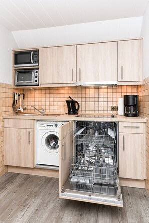 A compact kitchen with wooden cabinets, a microwave, a coffee maker, and a dishwasher.