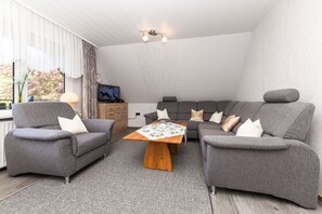 A modern living room with grey sofas, a wooden coffee table, and a TV on a wooden cabinet.
