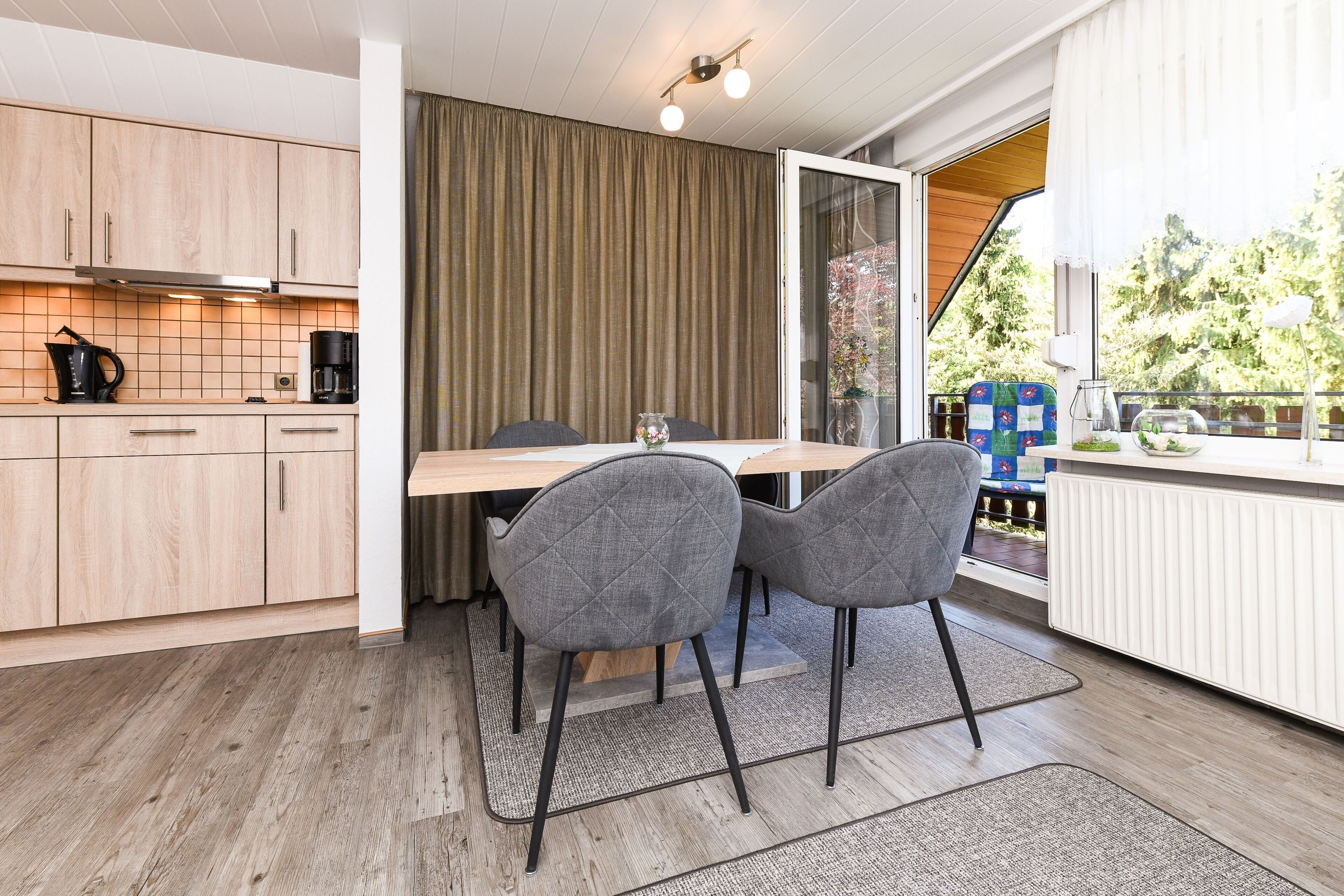 A modern kitchen with wooden cabinets, a dining table with two chairs, and a view of the outdoors through a sliding glass door.
