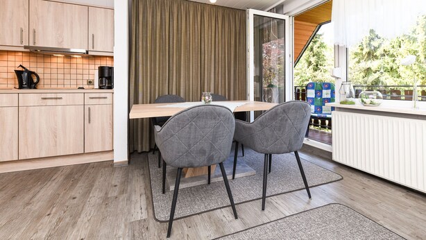 A modern kitchen with wooden cabinets, a dining table with two chairs, and a view of the outdoors through a sliding glass door.